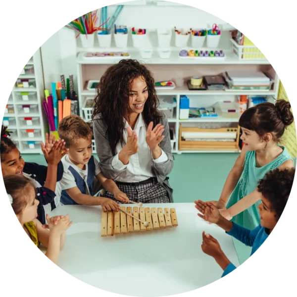 Teacher and Children with Xylophone Smiling teacher and young children clapping around a table with a wooden xylophone