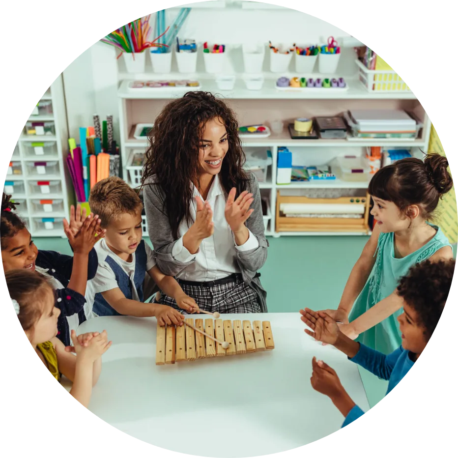 Teacher and Children with Xylophone Smiling teacher and young children clapping around a table with a wooden xylophone