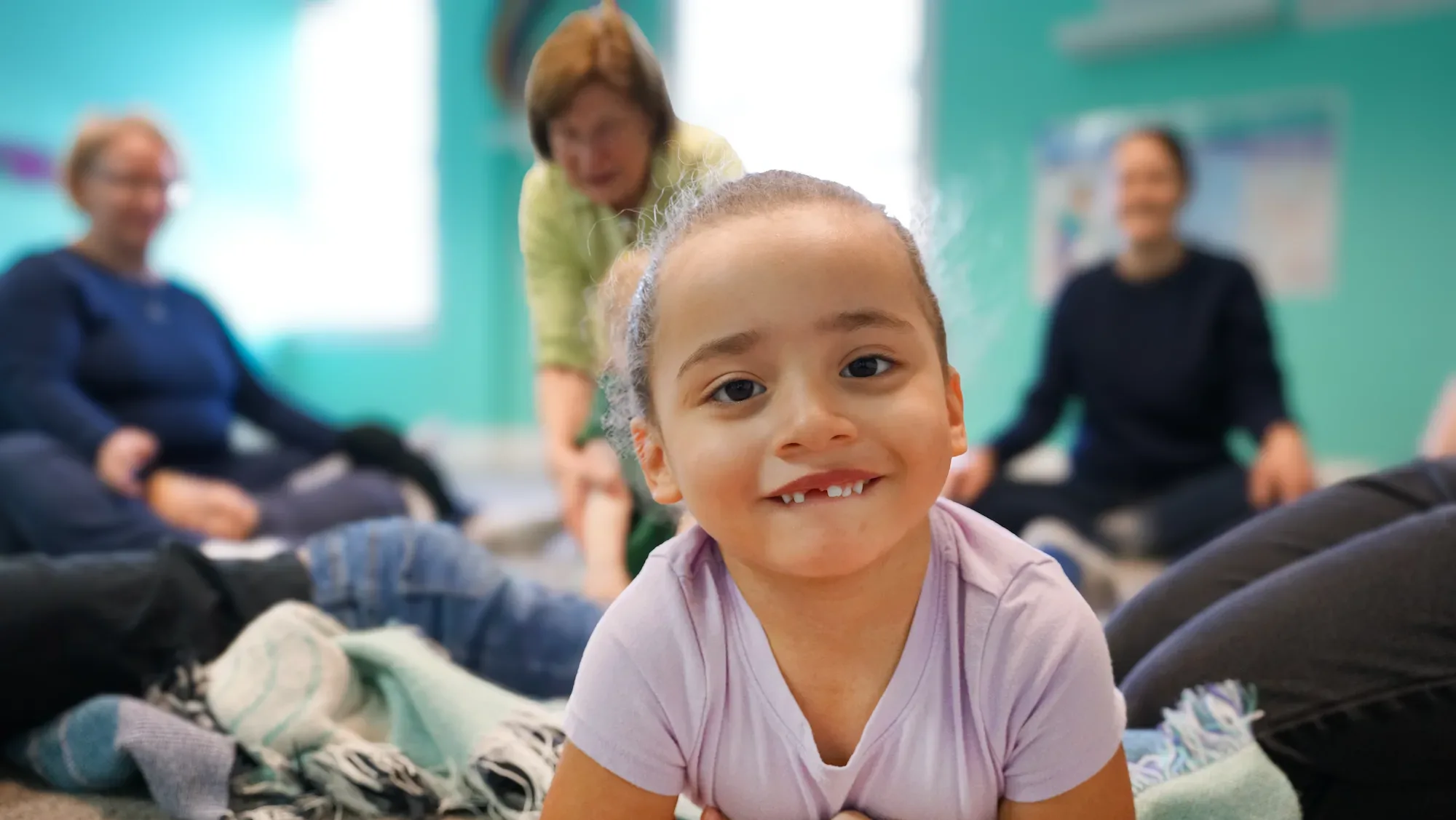 Young girl on floor smiling during music class. Smiling young girl lying on the floor during a music class, with adults in the background