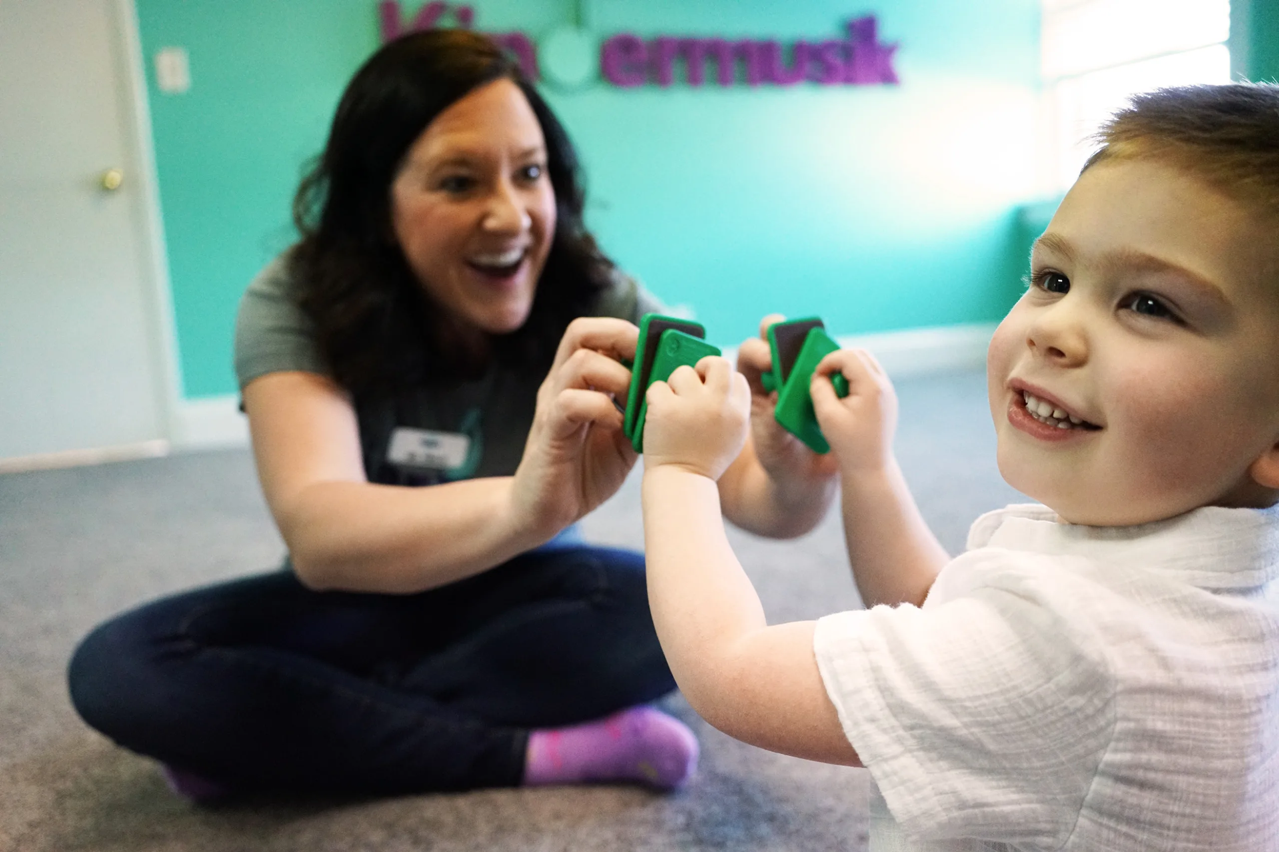 Educator And Preschooler With Hand Clappers A Kindermusik educator and a preschooler laughing together as they play small green hand clappers