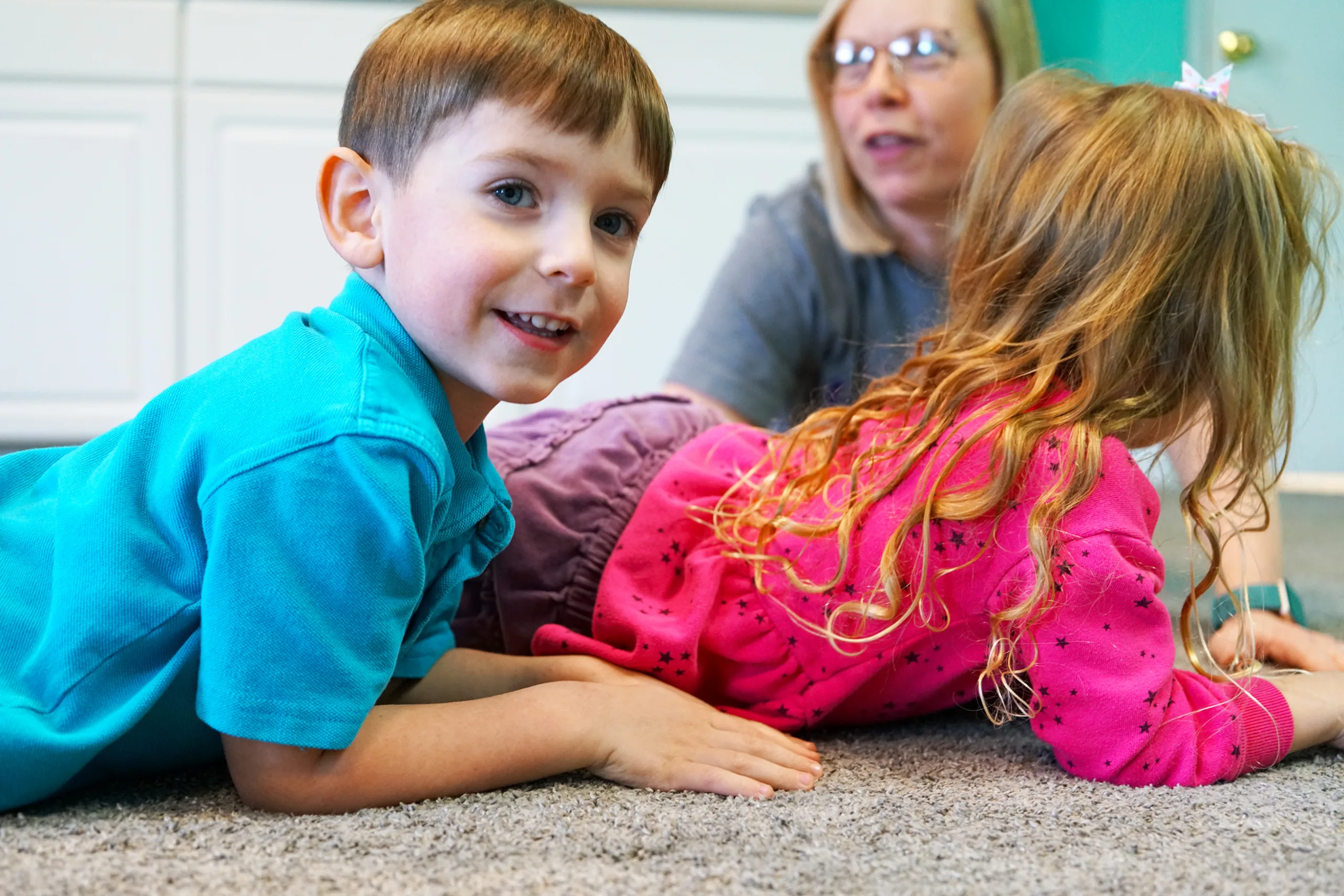 Preschoolers Lying On Classroom Carpet Two preschoolers lie on their tummies on the carpet, a smiling boy looking back at the camera