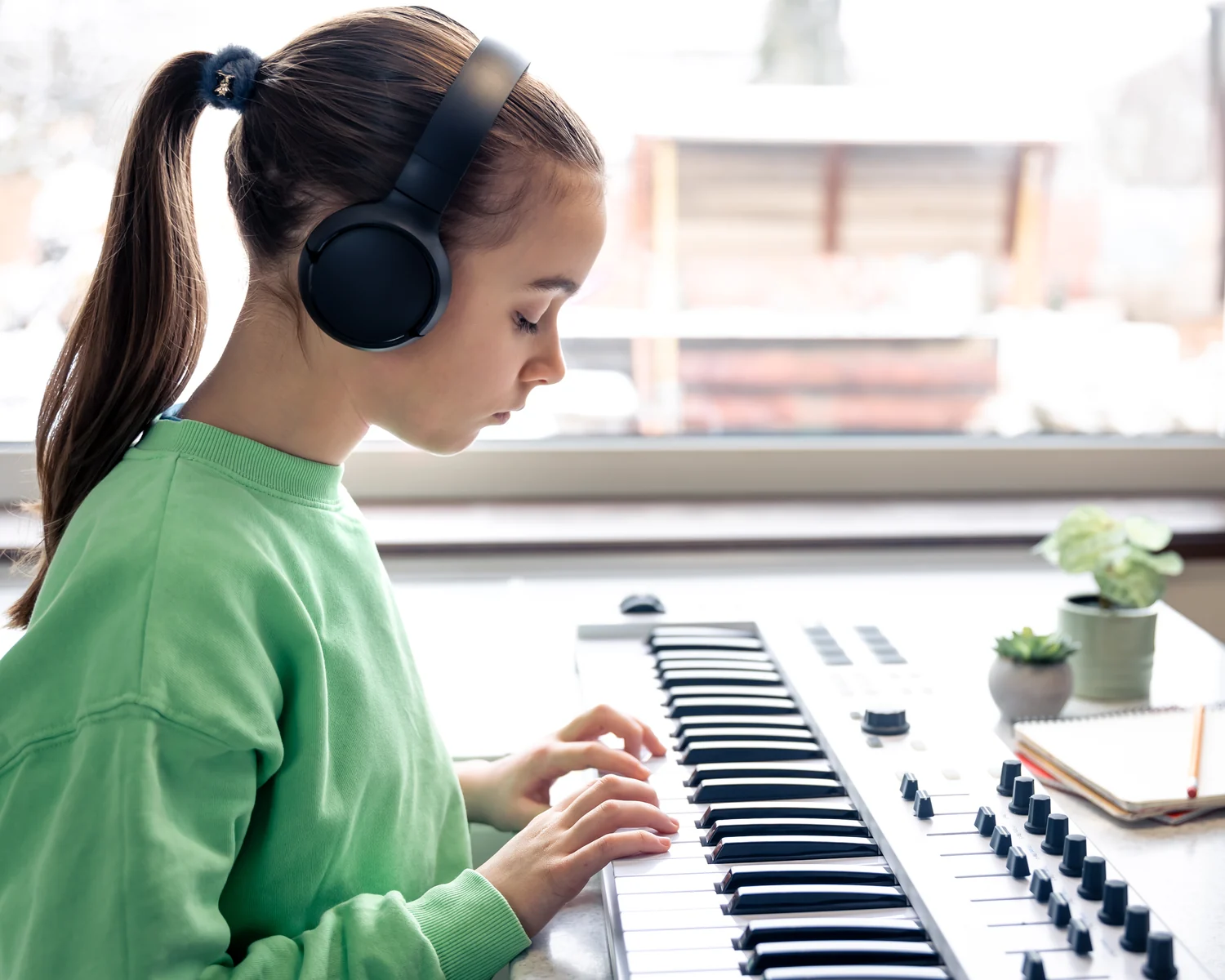 KeyNotes Student At Her Own Keyboard A school-age girl in headphones playing a digital keyboard by a bright window, a notebook and pencil beside her