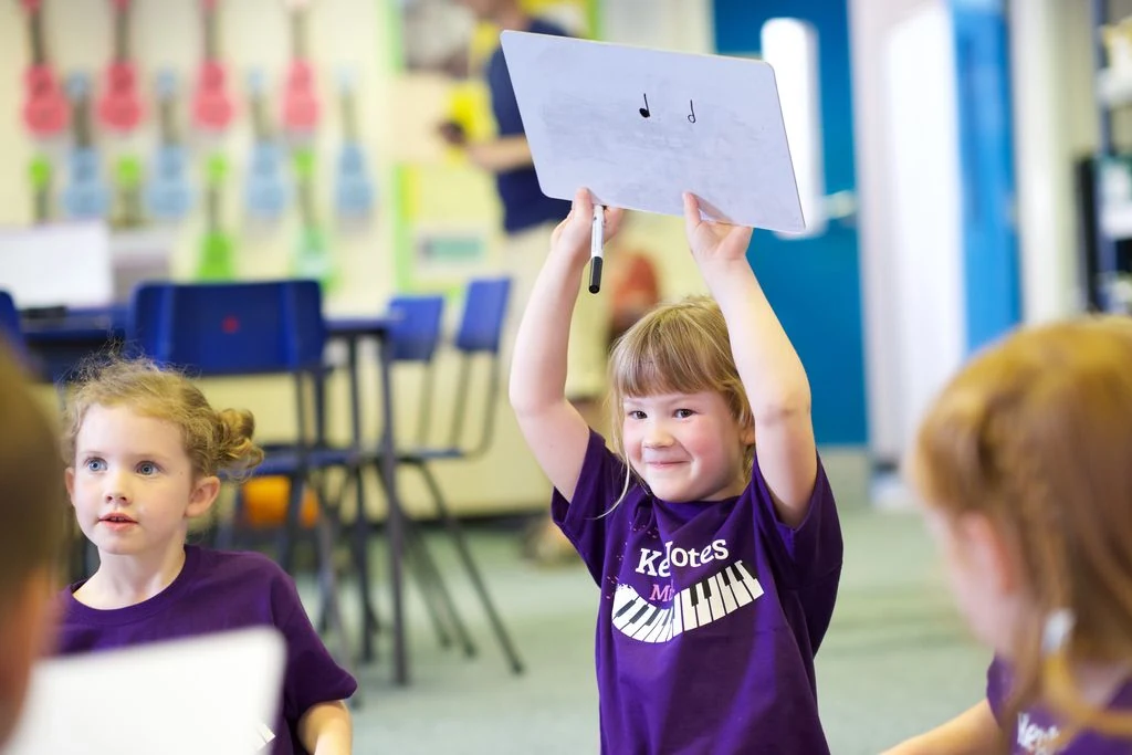 KeyNotes Student Showing Her Rhythm A young KeyNotes student smiling as she holds up a whiteboard showing a quarter note and a half note